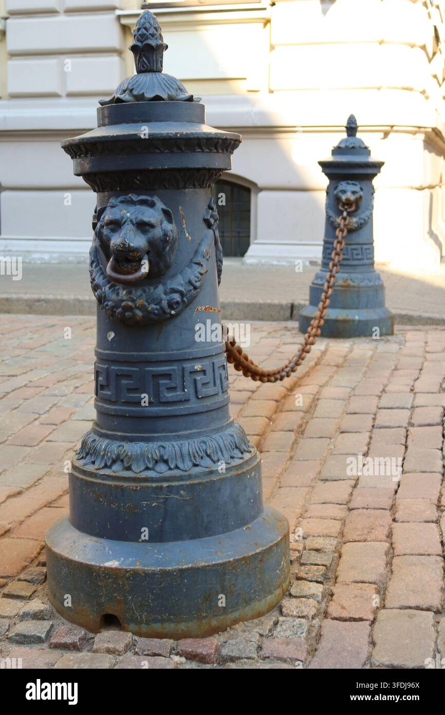 Verzierte schmiedeeiserne Löwenkopf-Pfosten, die durch Ketten verbunden sind, vor der Saeima, dem lettischen Parlamentsgebäude, in der Altstadt von Riga, Lettland. Stockfoto