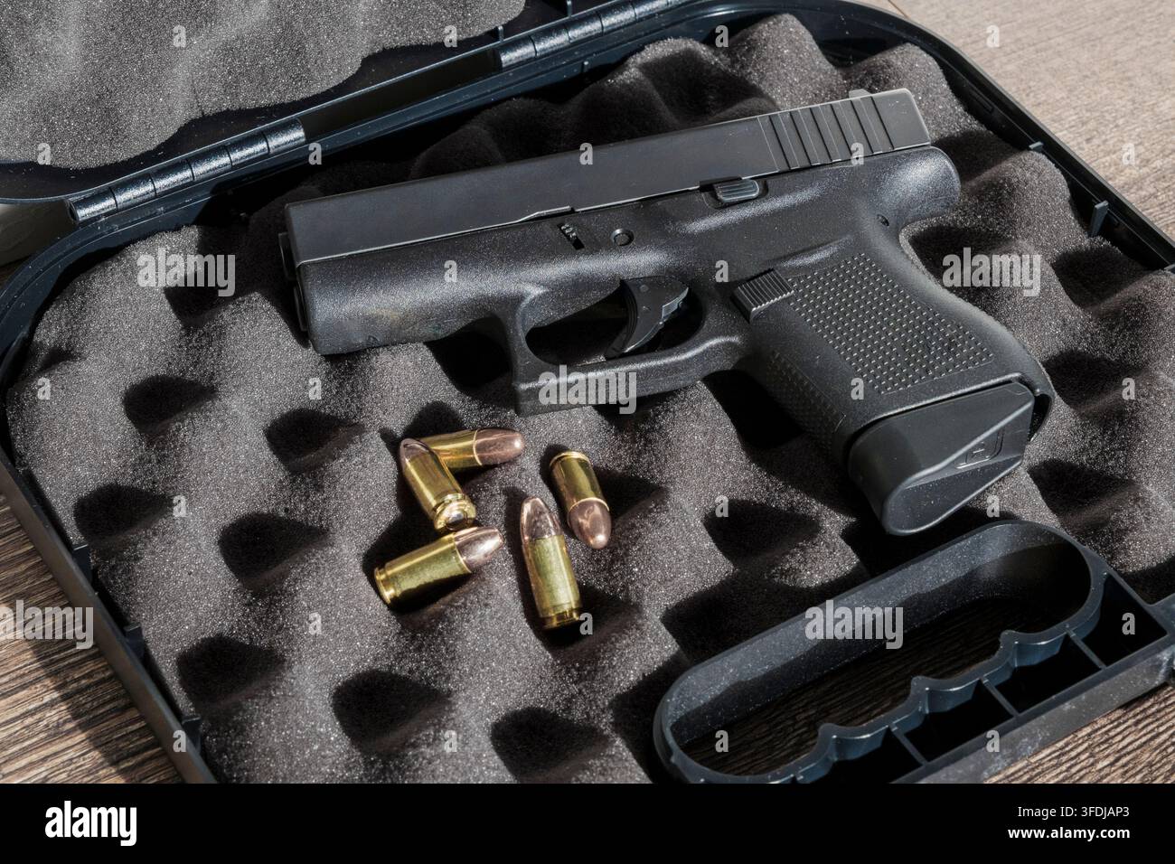 Eine halbautomatische Glock 43-Pistole ruht in einem schaumstoffgefütterten Hartkoffer neben vier losen 9-mm-Patronen und präsentiert so die Schusswaffe und ihre Munition. Stockfoto