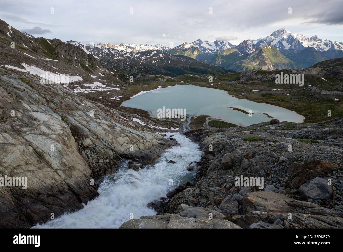 Blick auf einen Gletschersee und einen rauschenden Bach, der durch felsiges Gelände fließt, mit den schneebedeckten Gipfeln des Massiccio del Monte Bianco im Hintergrund Stockfoto