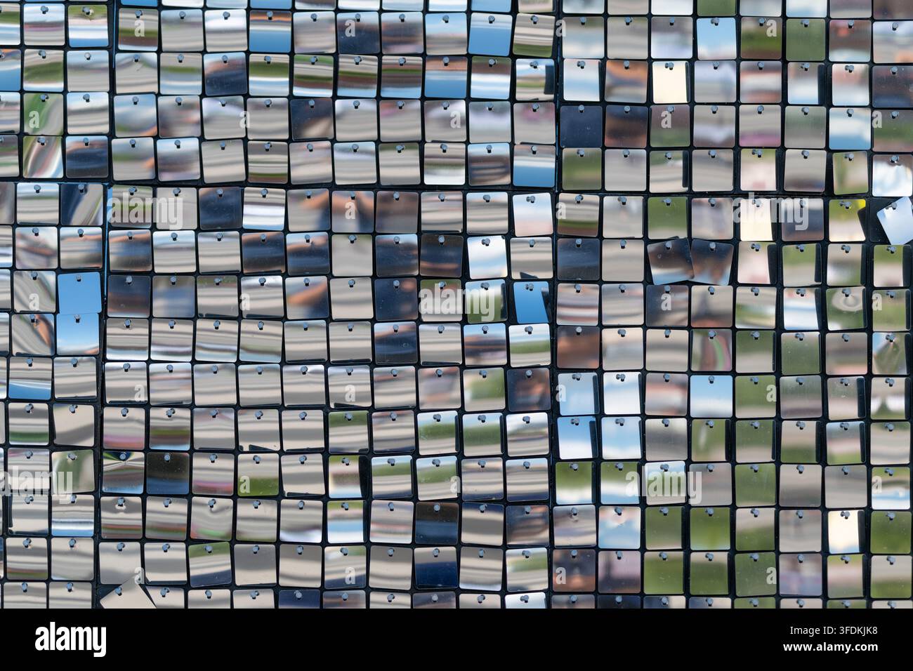 Eine atemberaubende Anordnung kleiner glänzender Quadrate fängt Sonnenlicht ein und erzeugt eine faszinierende Darstellung von Reflexionen. Die Umgebung fügt einen lebendigen Hintergrund hinzu, der das Bild bereichert Stockfoto