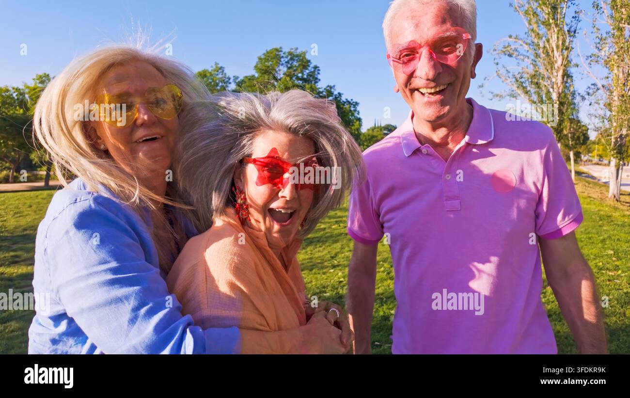 Drei fröhliche Seniorenfreunde tragen lustige Sonnenbrillen und genießen die Zeit im Freien Stockfoto