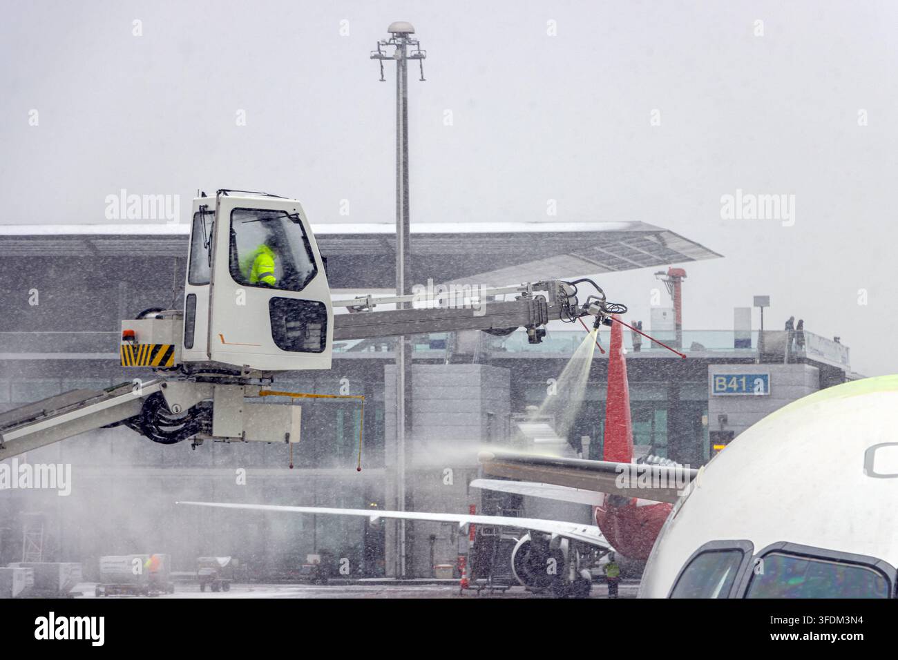 Bodenpersonal sprüht Enteisungsflüssigkeit auf den Heckflügel eines Flugzeugs während Wintereinsätzen Stockfoto
