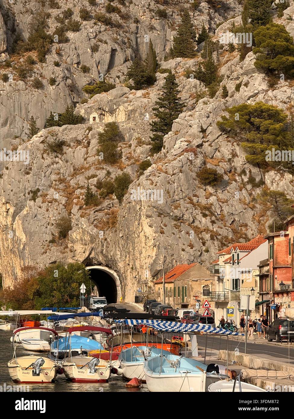 Boote, die im alten Stadtzentrum von Omiš vor Anker liegen, mit einem Tunnel im Hintergrund an der dalmatinischen Küste, Kroatien - Smartphone-aufgenommenes Stockfoto