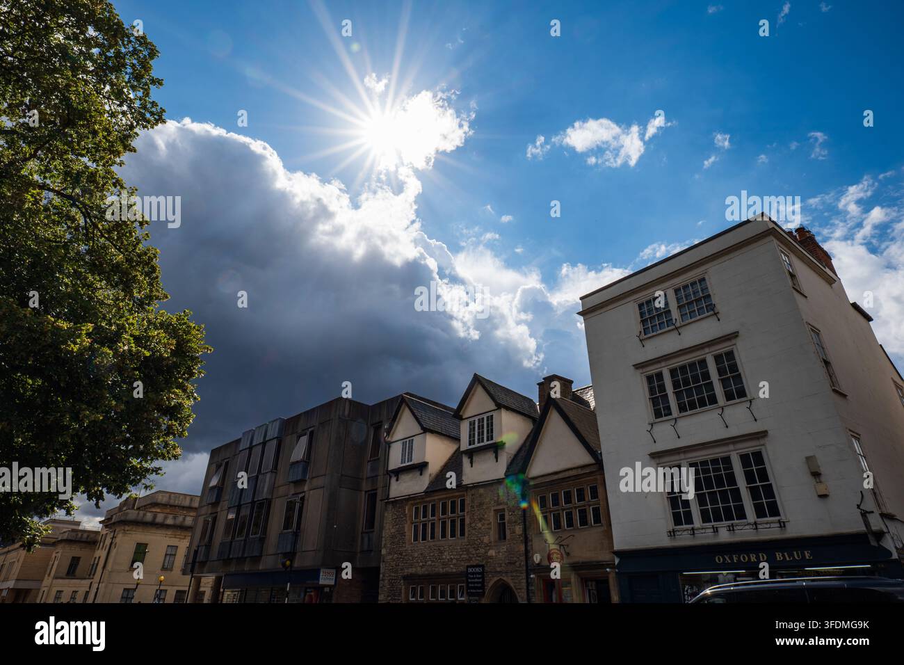 Oxford, Oxfordshire, England, 20. August 2026. Niedrigwinkelaufnahme von Ladenfronten entlang der St Aldate's Street mit einem Sonnenstrahlenburst und Wolken. Stockfoto