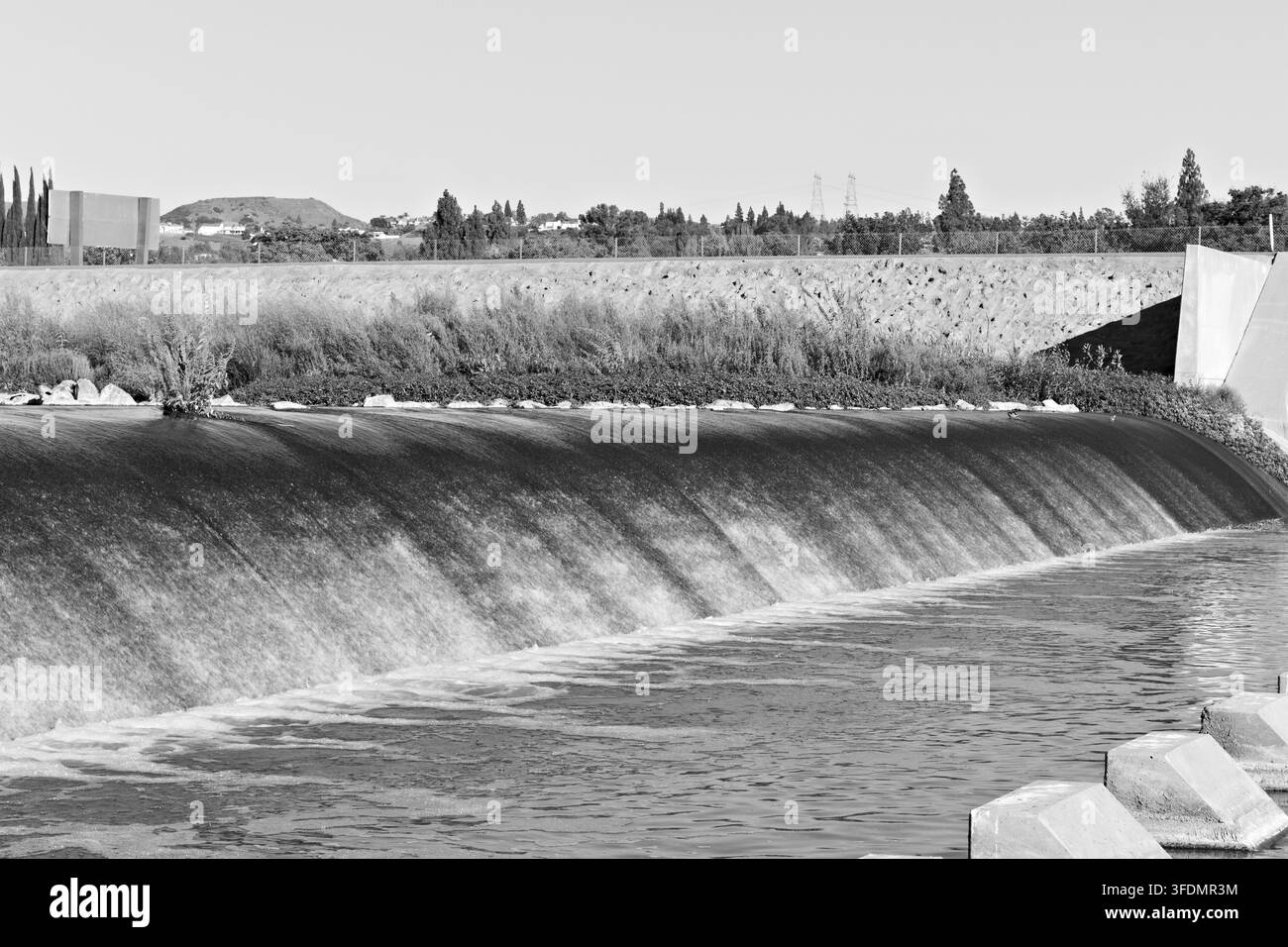 Wasser fließt über einen breiten Betongespeicher am Santa-Ana-Fluss, begrenzt von grüner Vegetation und Hochwasserschutzinfrastruktur in Yorba Linda. Stockfoto