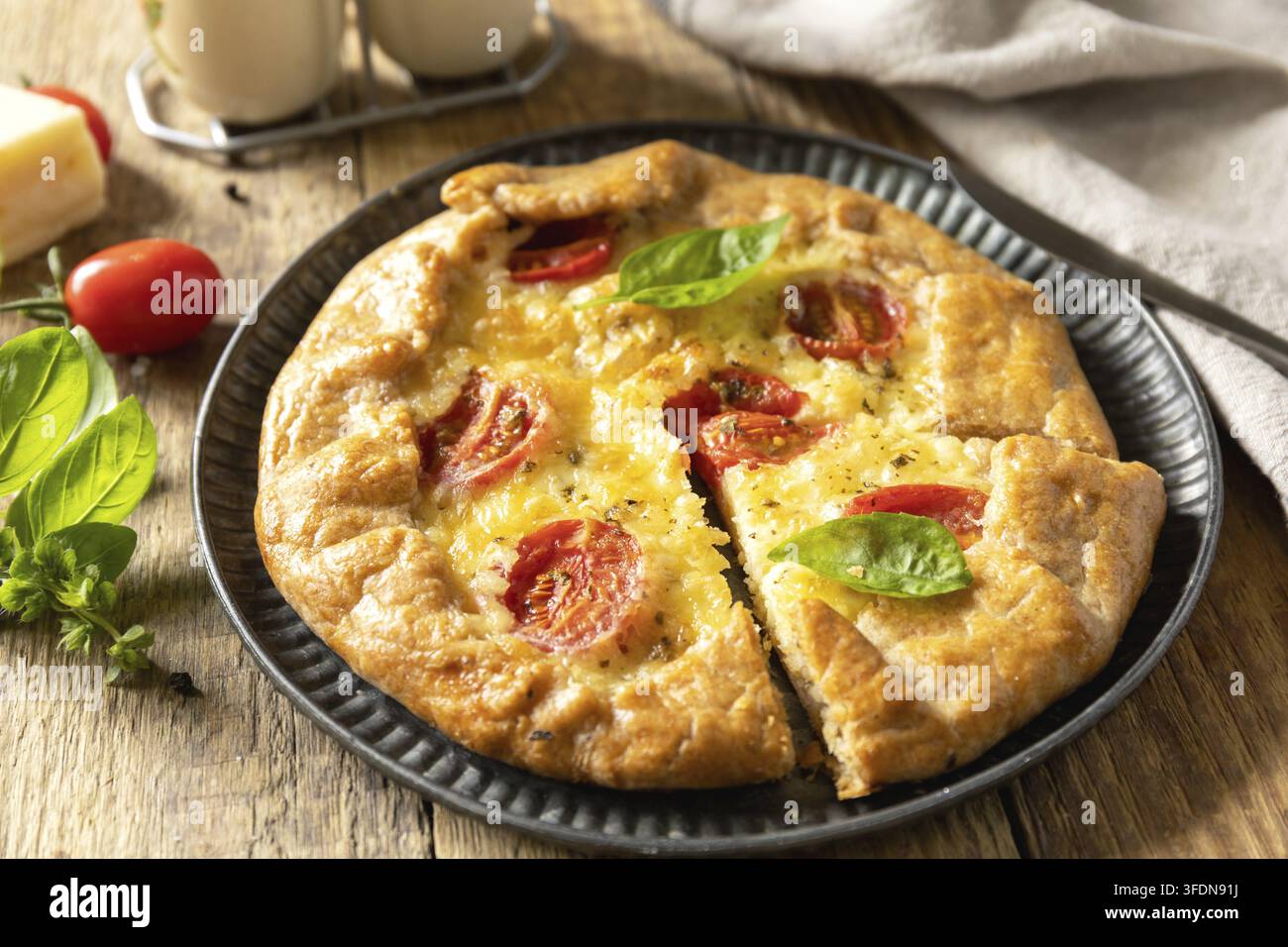 Knusprige Tomaten-Galette mit Adyghe-Käse und Kräutern auf rustikalem Hintergrund Stockfoto