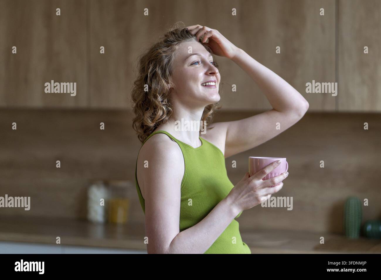 Lächelnde Frau in guter Stimmung begrüßt den neuen Tag, genießt den Morgen zu Hause, nippt an Kaffee, umarmt die entspannte Wochenendstimmung. Glückliche Frau fühlt sich dankbar, macht Stockfoto