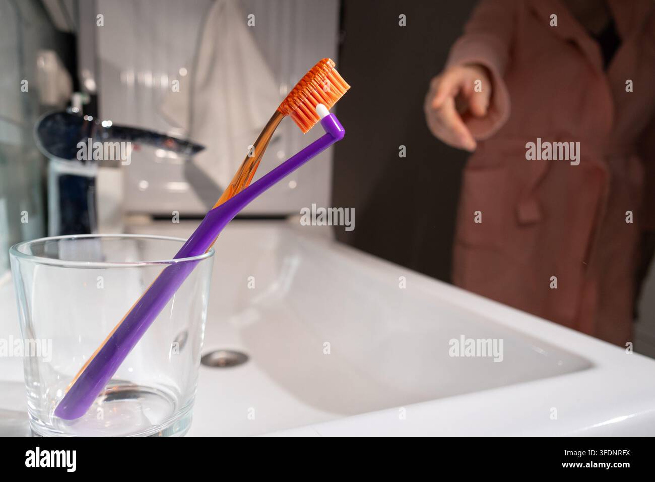 Eine Person wird gesehen, wie sie einen Zahnbürsten aus einem Glas voller Bürsten am Waschbecken im Badezimmer auswählt, was einen kleinen, alltäglichen Moment der persönlichen Hygiene illustriert Stockfoto