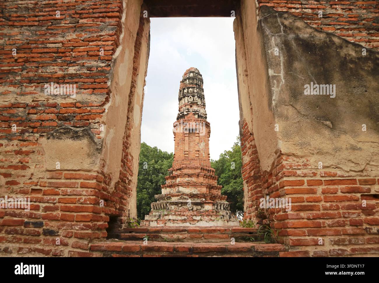 Kreative Bildkomposition eines alten Prang Chedi, gesehen durch den Ziegereingang der ruinierten Ordinationshalle im Wat Borom Phuttharam, Ayutthaya, Thailand Stockfoto