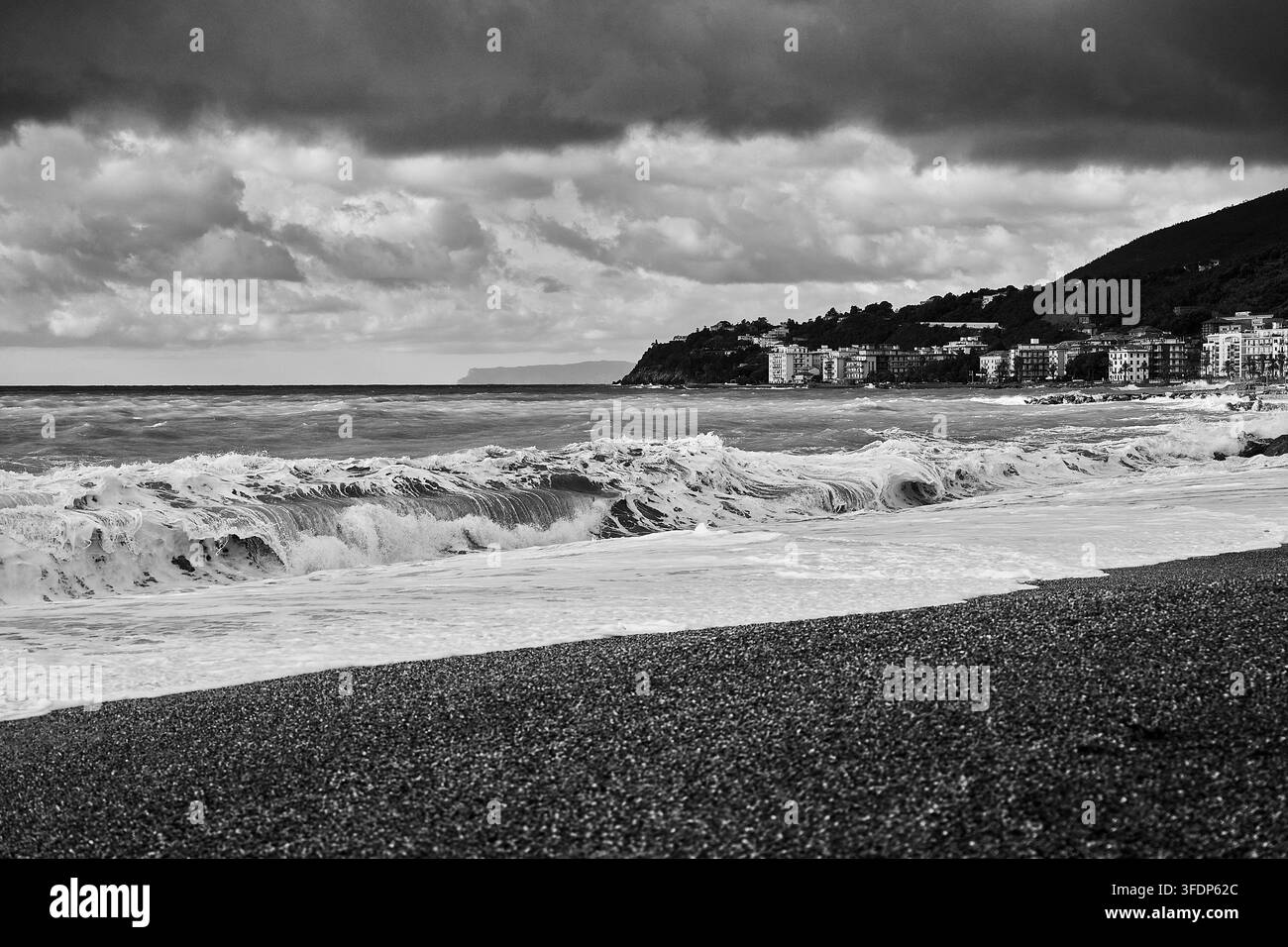 Kraftvolle Wellen, die an einem Kieselstrand entlang der ligurischen Küste unter dramatischen Sturmwolken in Schwarzweiß brechen, Italien. Stockfoto
