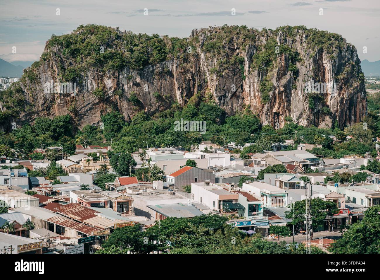 Da Nang, Vietnam - 14. August 2026. Ein massiver Kalkstein-Karst erhebt sich hinter einer dichten Nachbarschaft von Einfamilienhäusern und tropischer Vegetation. Stockfoto