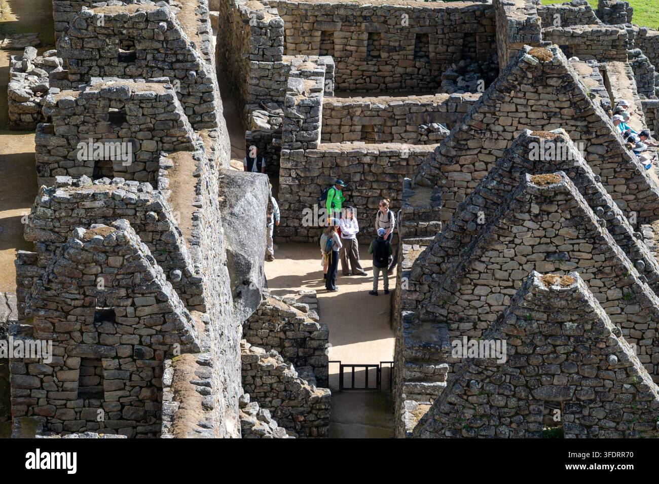 Besucher erkunden die alten Inka-Steinhäuser und engen Gassen von Machu Picchu in Peru, was Ehrfurcht, Geschichte und Abenteuer inmitten der gut erhaltenen Ruinen weckt Stockfoto