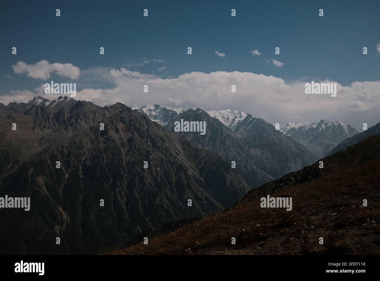 Schichtige Bergkämme, die sich unter weichen weißen Kumuluswolken über den Horizont erstrecken, ideal für Umwelt-, Ökologie- und Outdoor-Konzepte. Stockfoto