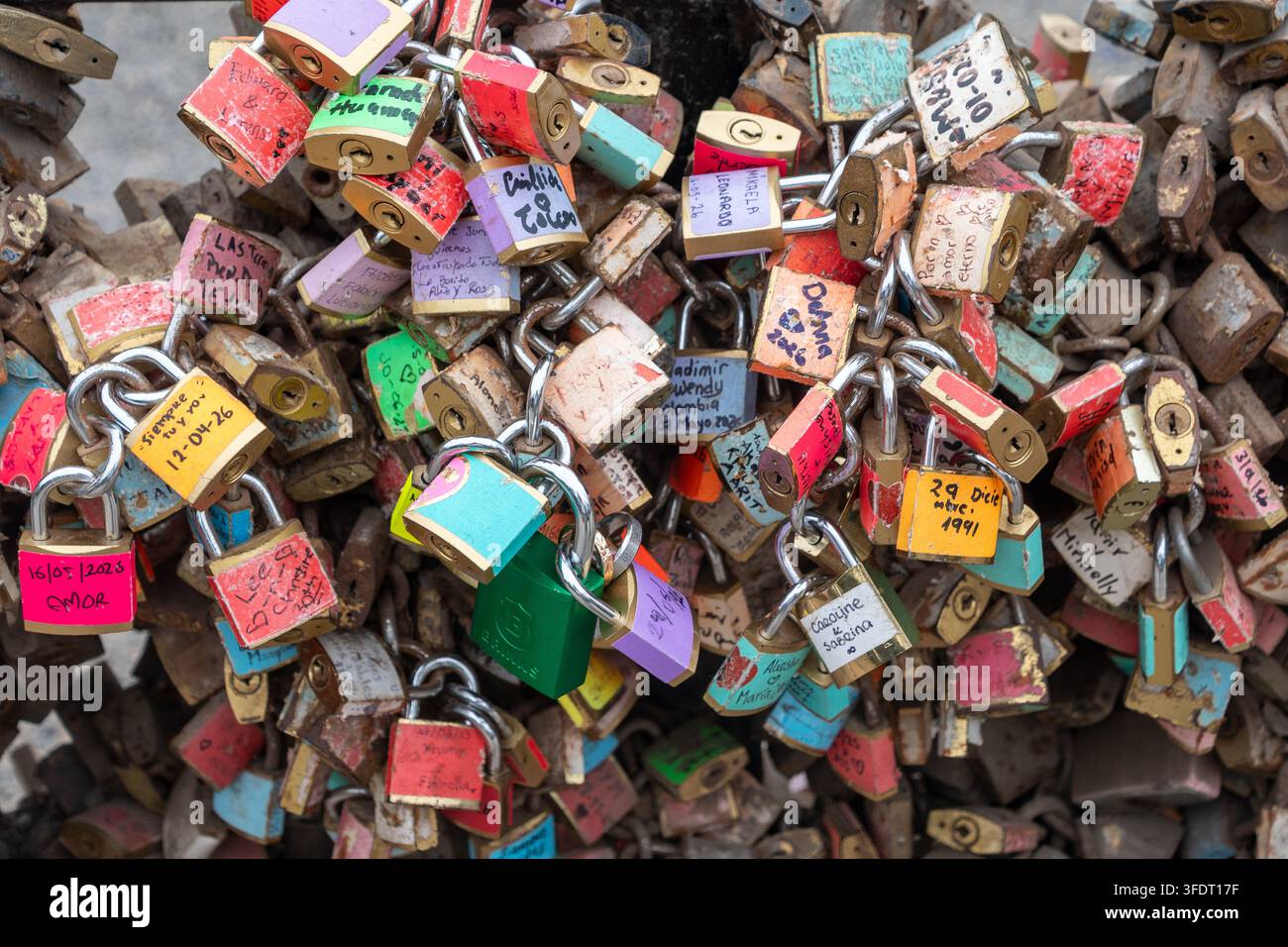 Ein dichter Cluster farbenfroher Vorhängeschlösser und handgeschriebener Liebesschlösser, die an einer Brückenketten befestigt sind, symbolisieren Romantik, Bindung, Erinnerungen und Reiseerinnerungen Stockfoto