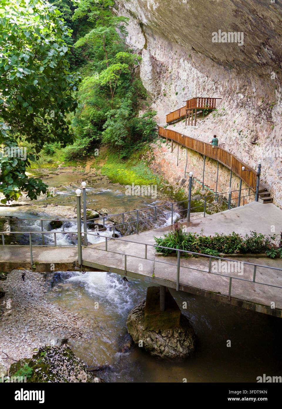 Ein malerischer Ausblick auf eine Schlucht mit einem fließenden Fluss und felsigen Stromschnellen. Eine Betonplattform mit Metallgeländern überquert das Wasser und führt zu einem Stockfoto