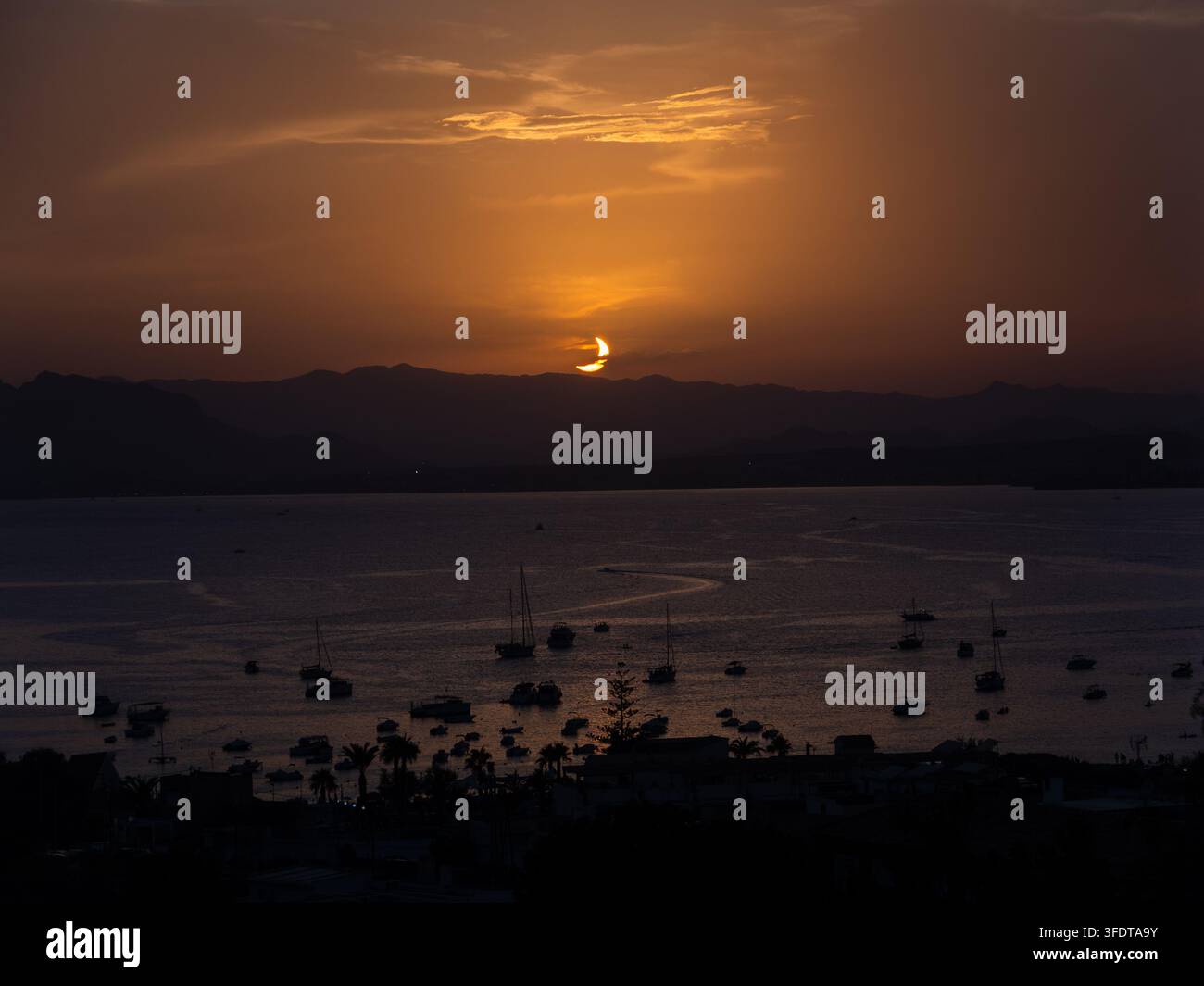 Teilweise Sonnenfinsternis während des Sonnenuntergangs über einem Hafen mit Booten, Spanien Stockfoto