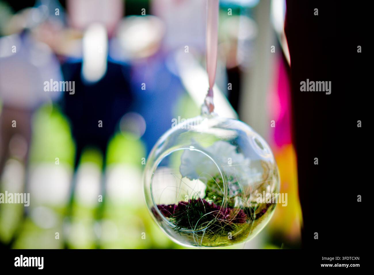 Dekorierter hängender Glas-Terrarien-Ornament als Teil einer eleganten Außengartenhochzeitsdekoration, mit verschwommenen Gästen im Hintergrund. Nützlich Stockfoto