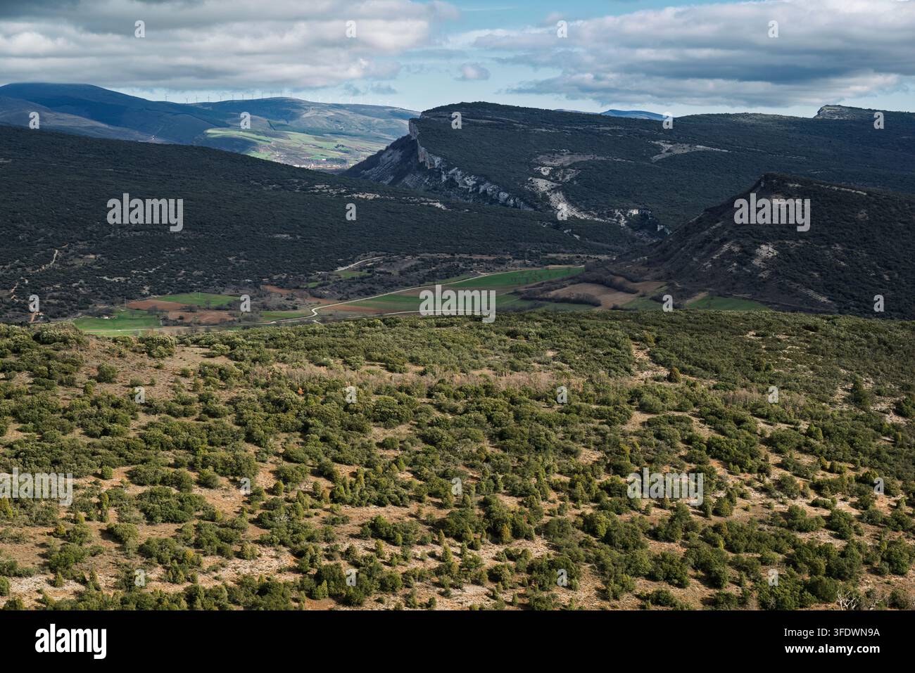 Rolle Berggipfel und grüne Täler in Kastilien und León, Burgos, Spanien, Europa, mit felsigen Klippen und entfernten Windrädern unter einem dramatischen Himmel. Stockfoto