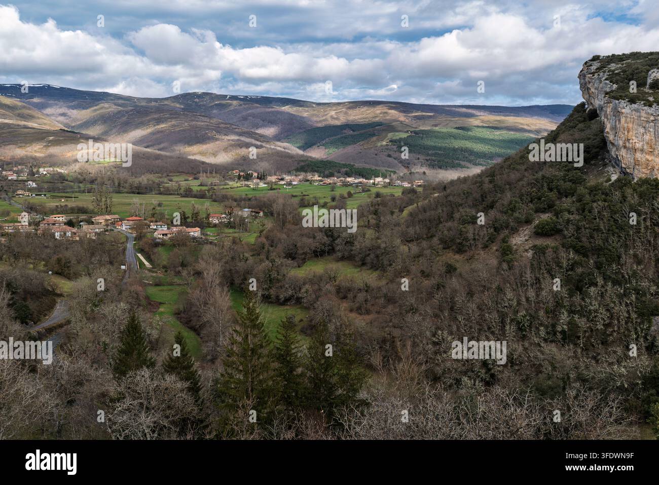 Blick auf das ländliche Tal in Burgos, Kastilien und León, Spanien, mit kleinen Dörfern, bewaldeten Hügeln und einer markanten Kalksteinklippe unter einer bewölkten Himmel Stockfoto