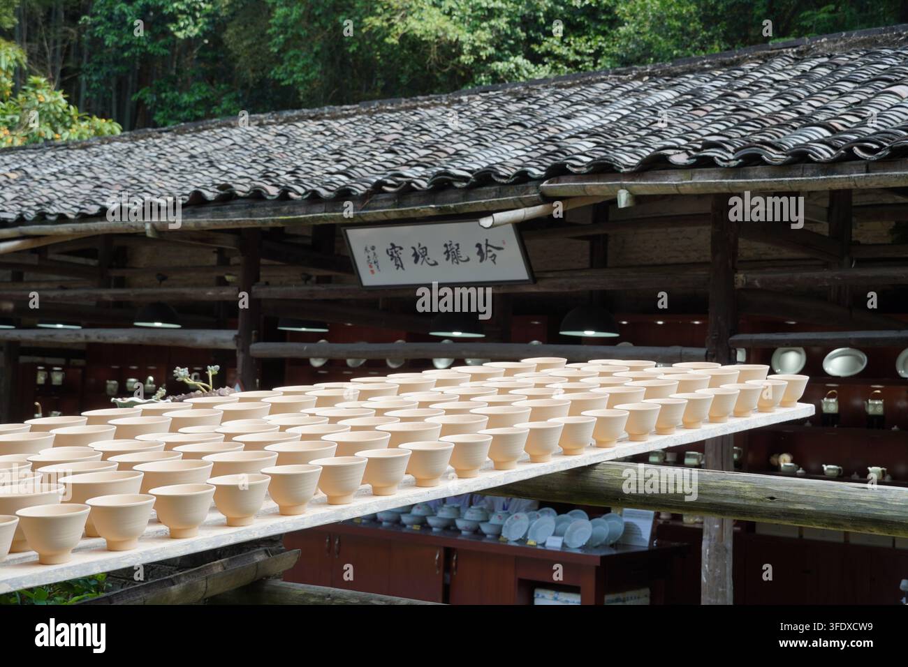 Reihen von ungebrannten Keramikschüsseln, die auf Gestellen unter einem Ziegeldach in einer Töpferwerkstatt in Jingdezhen, China, trocknen Stockfoto