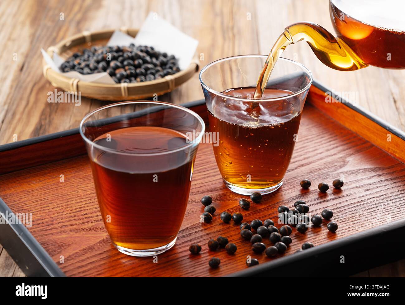 Eiskalter schwarzer Sojathee aus dem Glasteebeutel in ein Glas auf Holztablett gießen Stockfoto