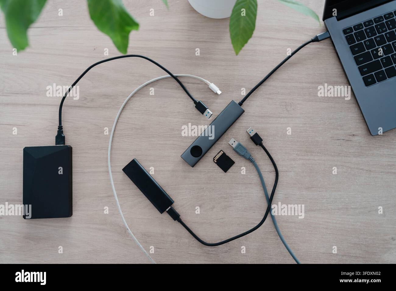 Aluminium-USB-Hub verbindet einen Laptop mit einer externen Festplatte, einem tragbaren SSD, einer Speicherkarte und Kabeln auf einem Holzschreibtisch. Porterweiterung und zusätzliche Steckplätze Stockfoto
