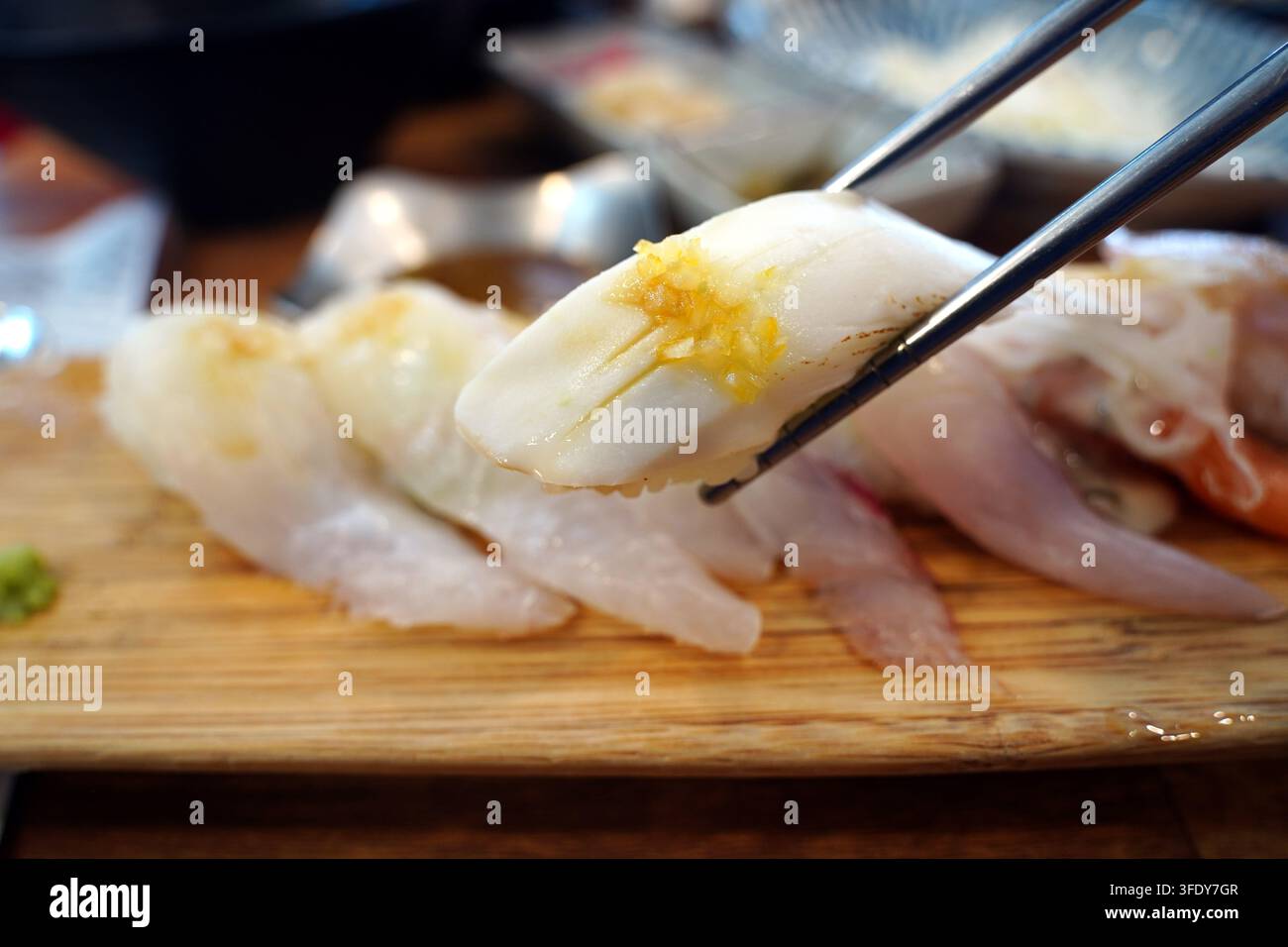 Frischer weißer Fisch-Sushi, der mit Stäbchen über einem Holzbrett gehalten wird, Nahaufnahme Stockfoto