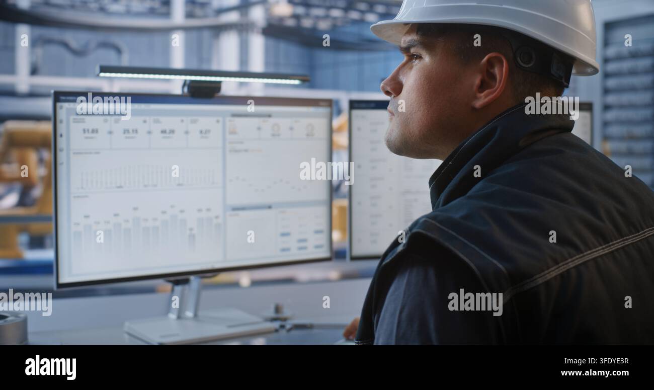 Industriemechaniker tippt auf Tastatur, inspiziert CAD-Modell eines Autochassis auf Desktop-Anzeige in einer High-Tech-Anlage. Robotikintegration treibt den digitalen Übergang der modernen Smart Factory voran. KI-Fertigung. Stockfoto