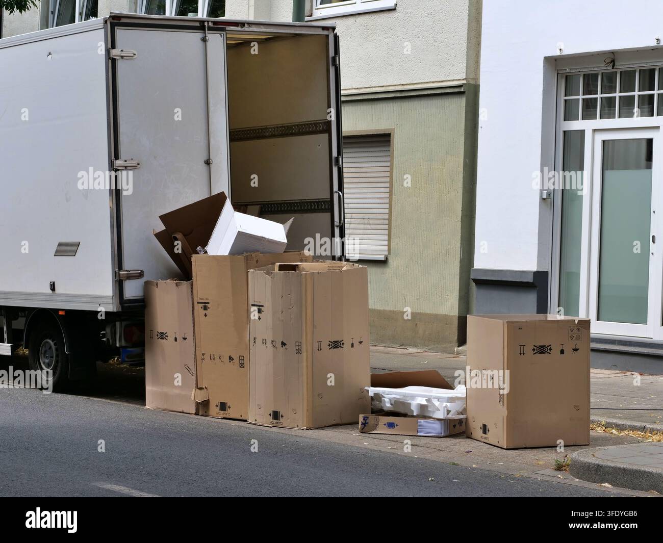 Offener Lieferwagen, der entlang eines städtischen Wohngebäudes geparkt ist, mit verschiedenen Pappkartons, Styropor und Abfallmaterialien, die auf dem Bürgersteig gestapelt sind. S Stockfoto