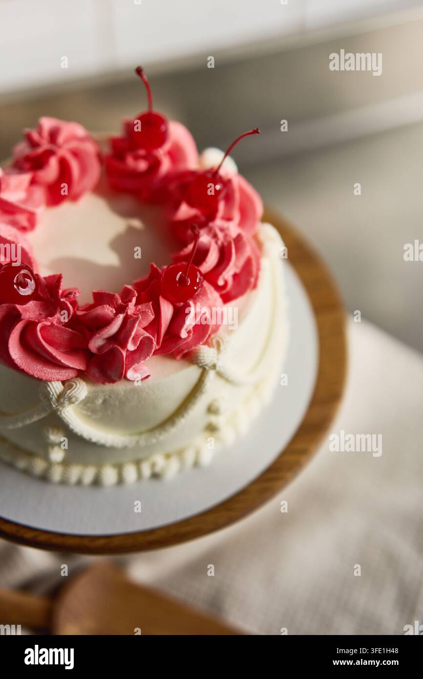 Runder Festkuchendekorierter Kuchen mit rosa Buttercreme-Rosetten, glänzenden Maraschino-Kirschen, gerohrter Zuckerglasur und glattem weißem Zuckerguss auf Holzständer, mit Stockfoto