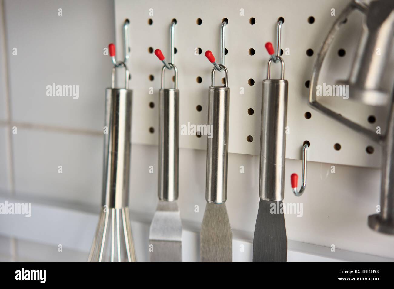 Edelstahl-Küchenutensilien, die an einem Steckbrett mit rotkappen Haken hängen, Nahaufnahme, mit Küche, Utensil, Edelstahl-Detail, zeigt Griff Stockfoto