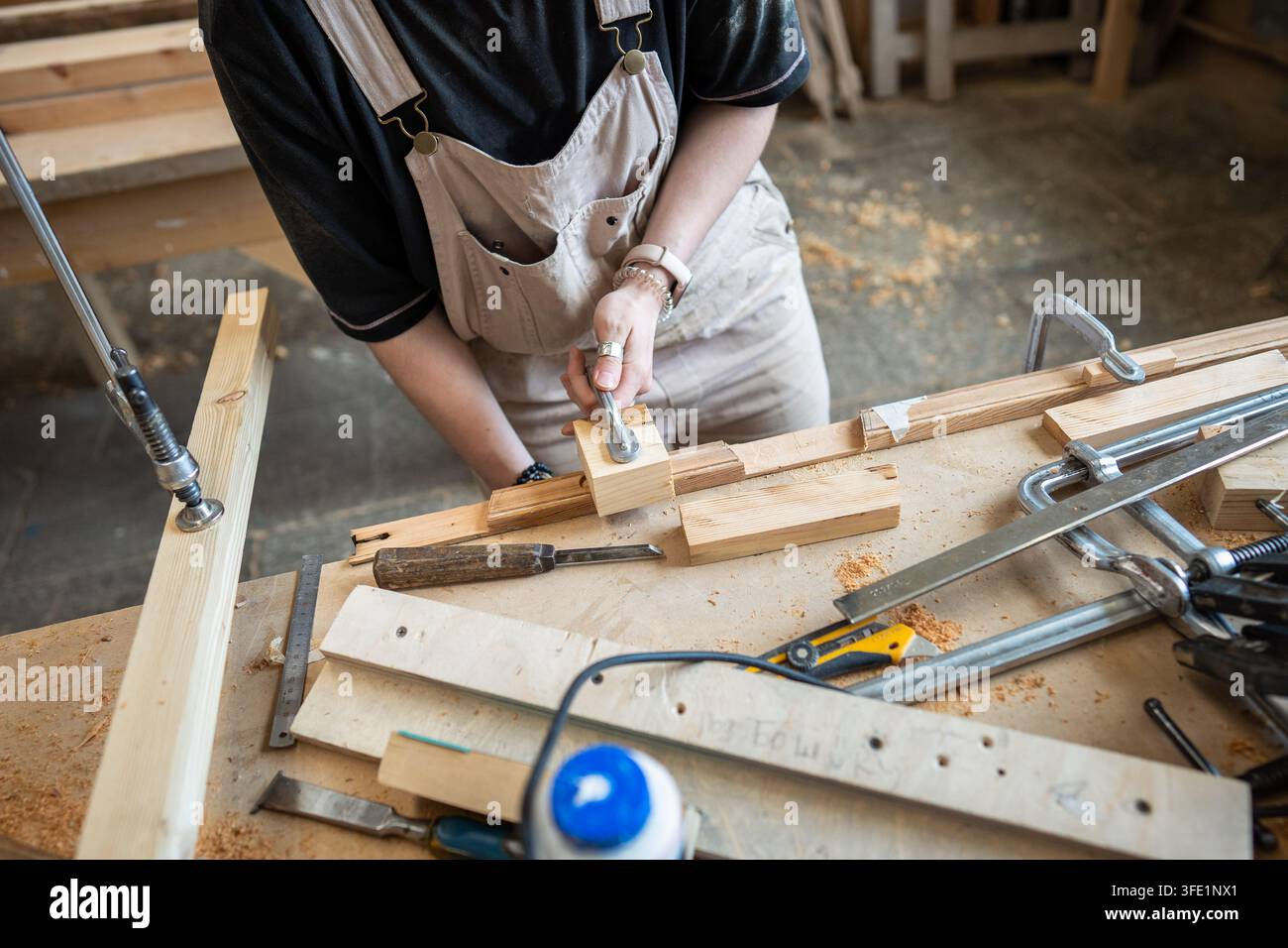 Handwerkerin arbeitet mit Holzblöcken und Werkzeugen an einer Werkbank in einer Restaurierungswerkstatt Stockfoto