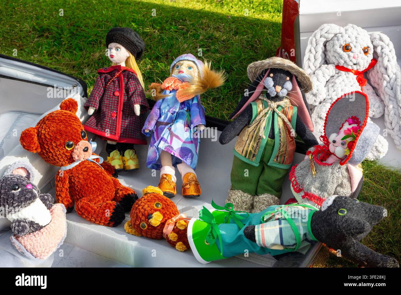 Ein offener Koffer und eine Außenvitrine gefüllt mit einer bunten Auswahl an handgefertigten Kunsthandwerkerpuppen und Plüschtiere, mit stilvoll gekleideten Modepuppen Stockfoto