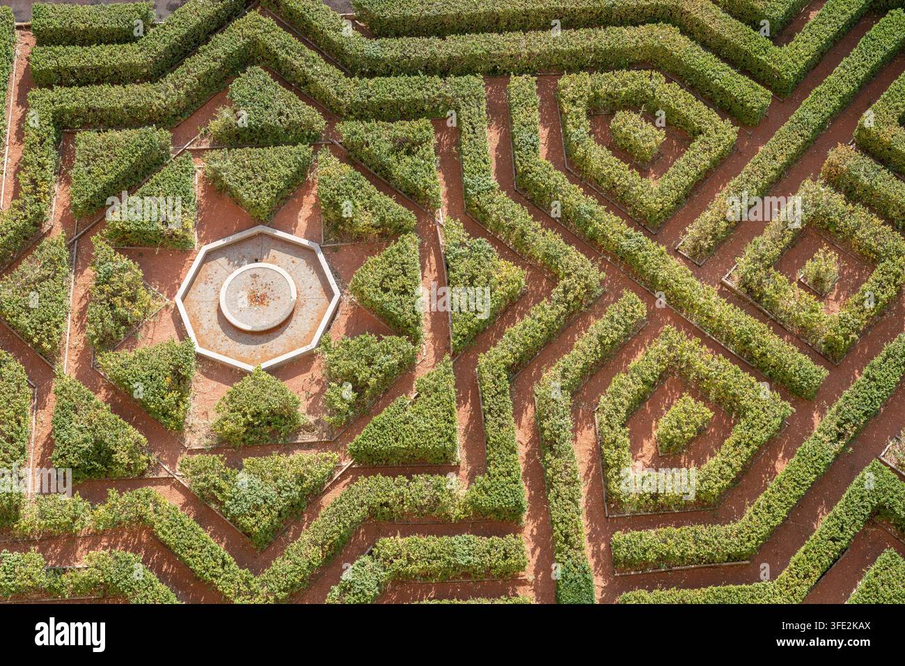 Luftaufnahme eines formalen geometrischen Hecken Gartens mit einem zentralen achteckigen Brunnen, gepflegten Wegen und symmetrischen Mustern. Warme Erdtöne Stockfoto