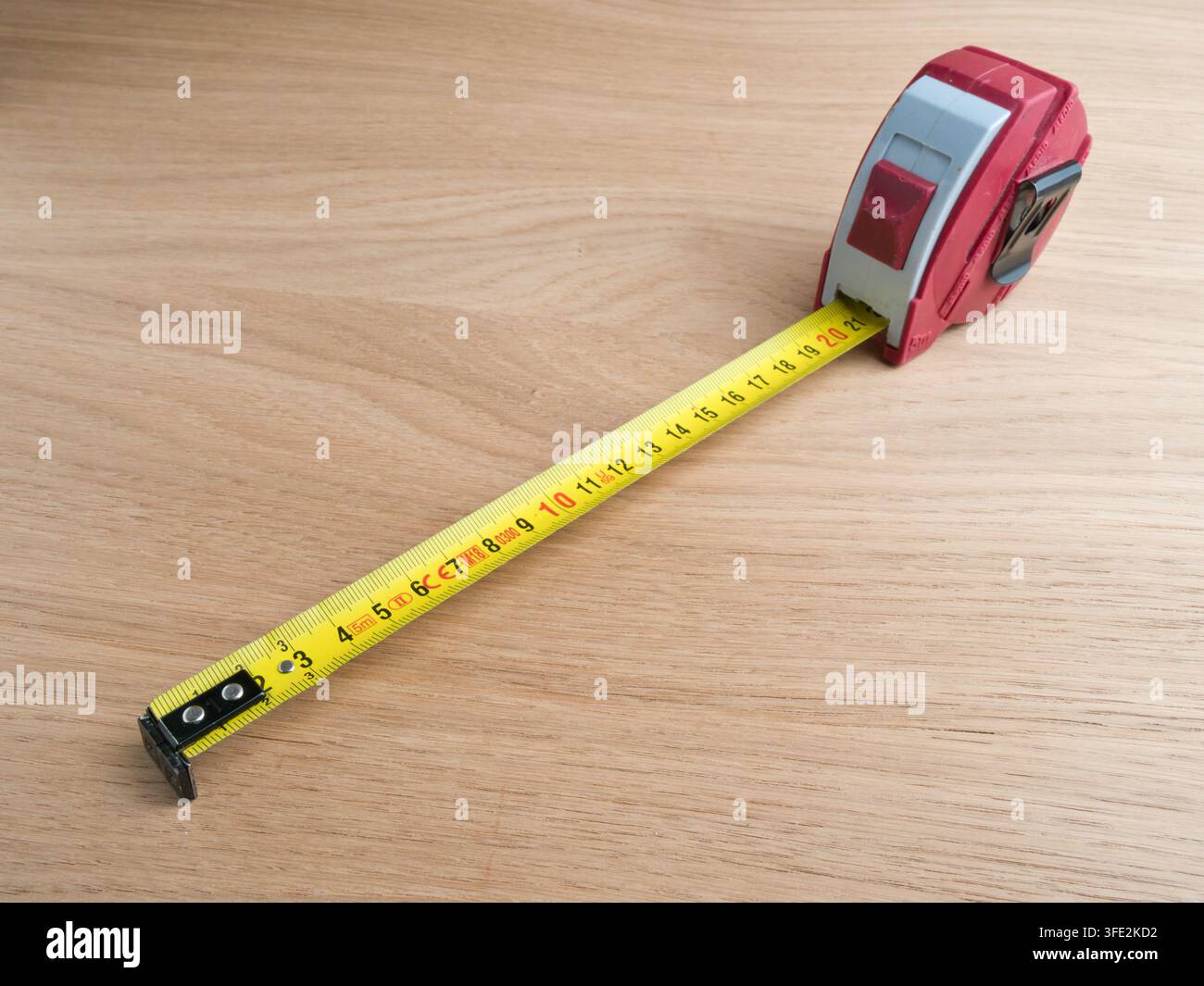 Rotes Messband auf Holz ausgezogen – Ein rot-graues einziehbares Messband, vollständig auf einer hellen Holzoberfläche ausgezogen, mit metrischen Markierungen. Stockfoto
