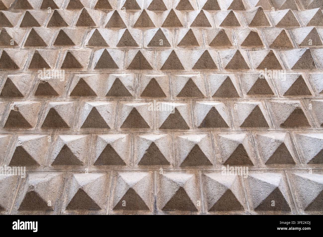 Historische rustizierte Steinmauer mit sich wiederholenden Pyramidenblöcken, die ein strukturiertes geometrisches Muster an einer architektonischen Fassade in Segovia, Spanien, bilden. Neutr Stockfoto