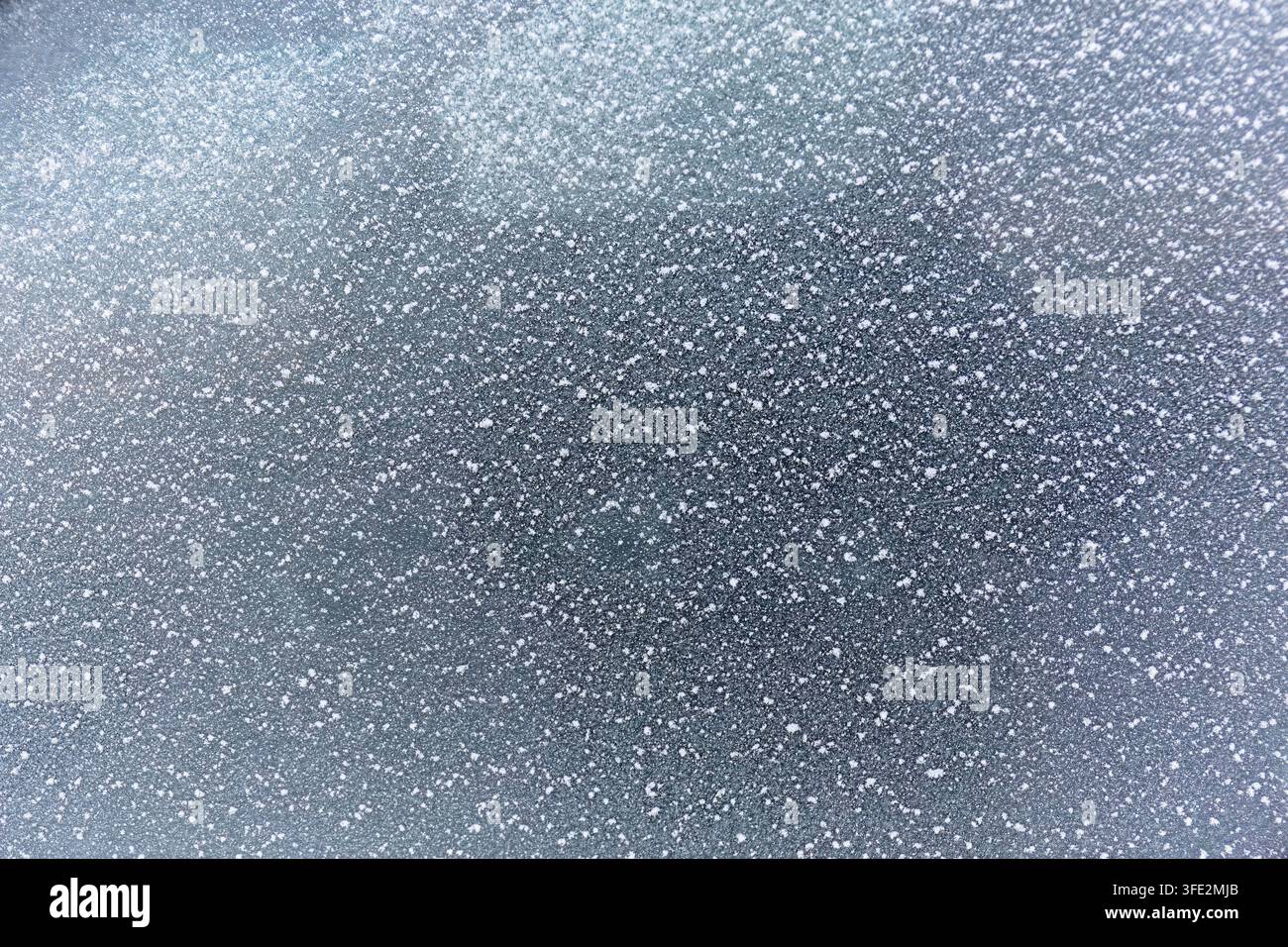 Eisige Glasverwandlung verwandelt eine Autofenster in ein Feld feiner weißer Eiskristalle und dunkler reflektierter Formen, wodurch ein abstrakter Winter entsteht Stockfoto