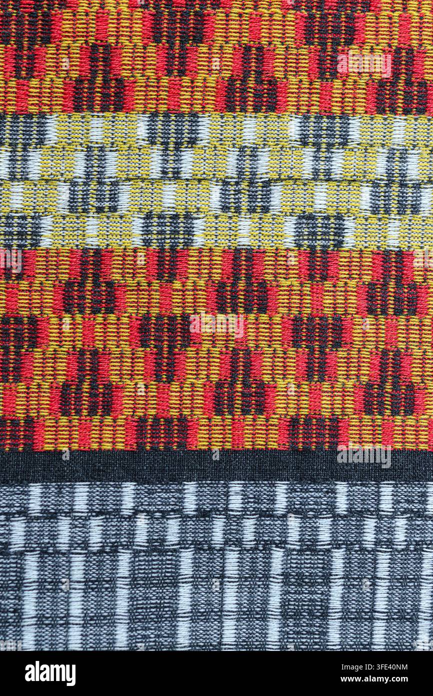 Nahaufnahme von handgewebtem Mudmee-Ikat-Stoff mit einem roten, gelben, schwarzen und grauen geometrischen Muster, fotografiert in Thailand. Stockfoto