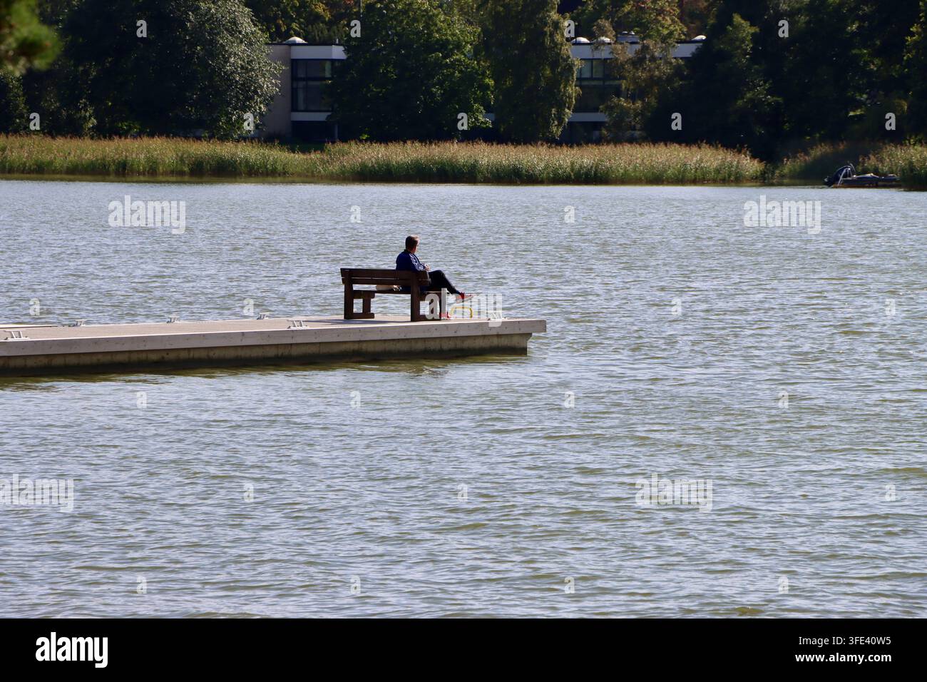 Mann sitzt auf einem Pier an der Laajalahti-Bucht bei Munkkiniemi, Helsinki, Finnland, am 21. August 2026 Stockfoto