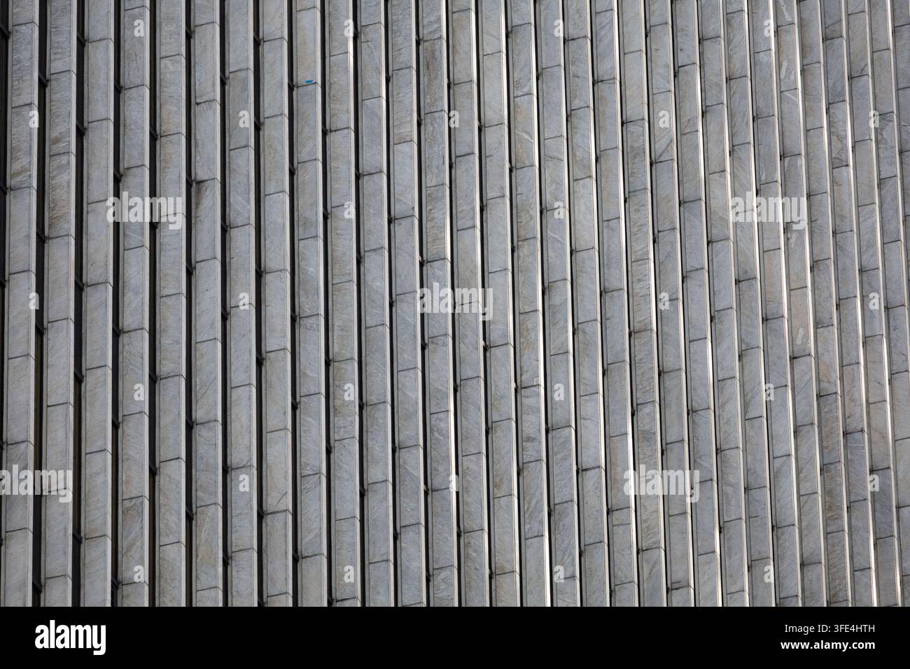 Nahaufnahme einer grauen Gebäudefassade mit sich wiederholenden vertikalen architektonischen Elementen, die ein minimalistisches geometrisches Muster bilden. Stockfoto