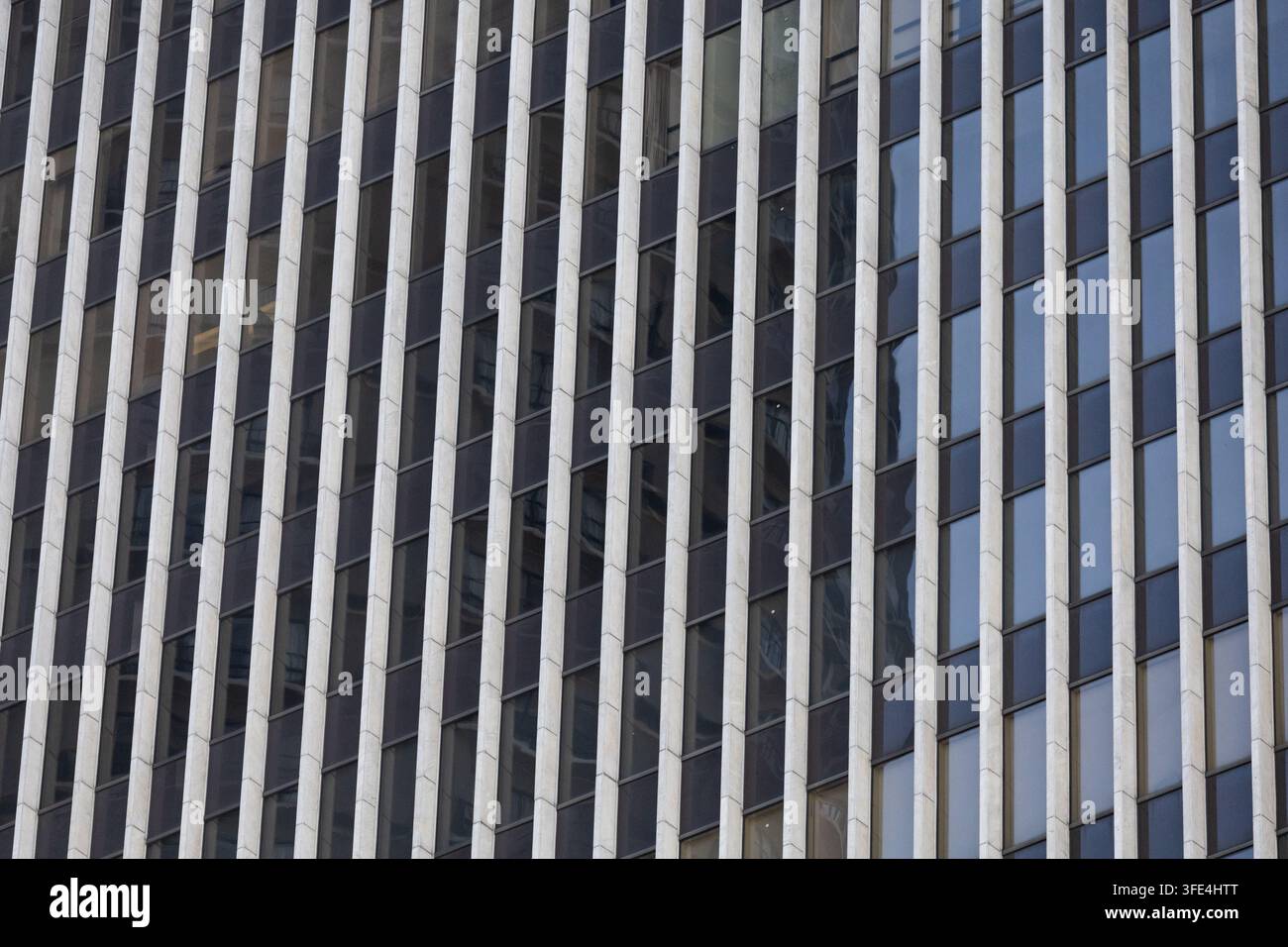 Nahaufnahme einer modernen Gebäudefassade mit sich wiederholenden vertikalen strukturellen Elementen und dunklen Fenstern, die ein geometrisches architektonisches Muster bilden. Stockfoto