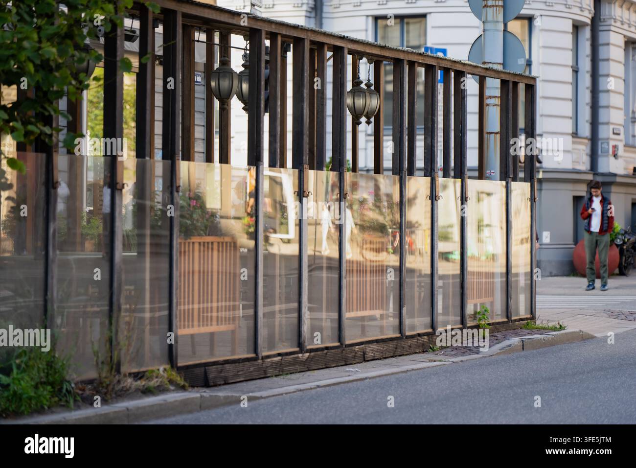 Reflexionen nahegelegener Gebäude spiegeln sich in einem Glas- und Metall-Straßengitter wider, einer kostengünstigen Lärmschutzlösung, die es Rigaer Cafés und Bars ermöglicht, Tische nebenan offen zu halten Stockfoto