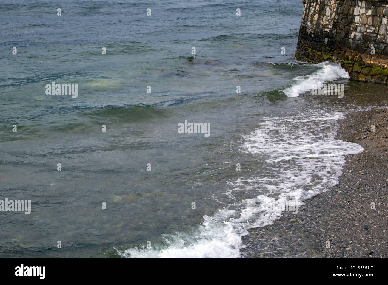 Das felsige Ufer des Comer Sees. Das Wasser ist unruhig und wellig Stockfoto