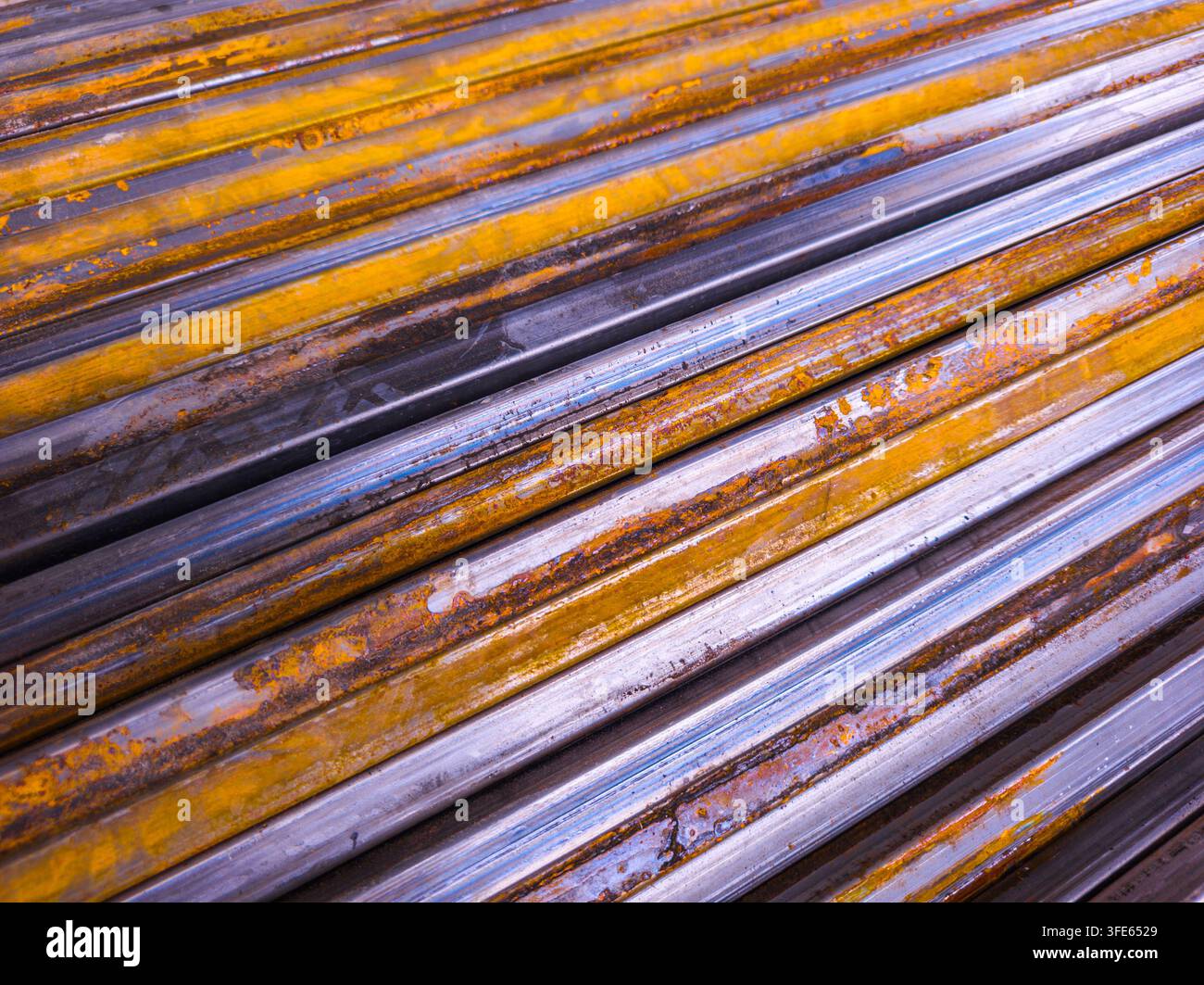 Nahaufnahme von gestapelten Metallrohren, die erhebliche Verwitterung zeigen. Die Rohre weisen silberne Töne mit gelben Flecken und Rost auf und betonen industriellen Verfall. Stockfoto