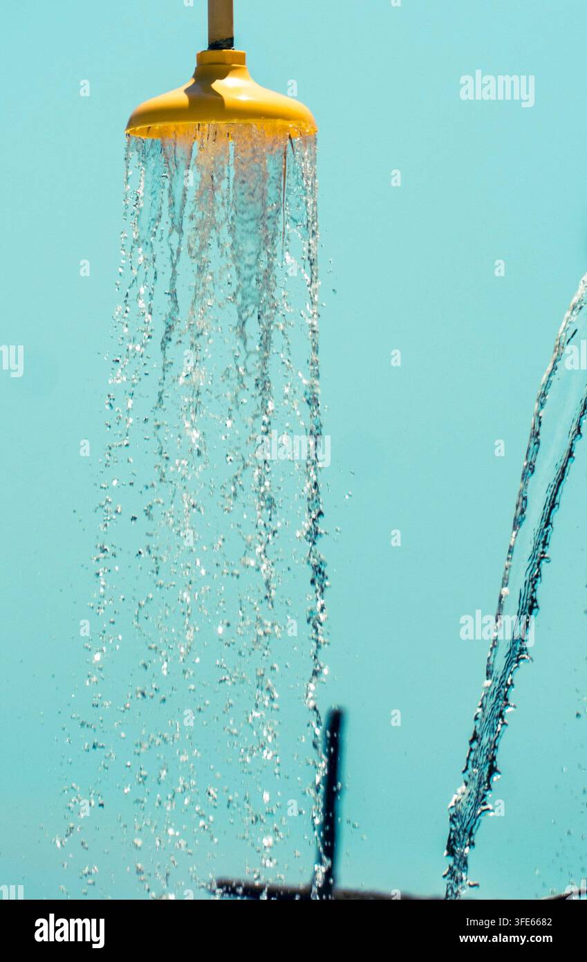 Gelber Außenduschkopf mit fallenden Wasserströmen vor einem türkisblauen Hintergrund. Stockfoto