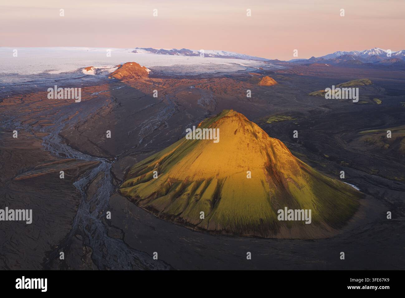 Luftaufnahme des Maelifell-Vulkans mit seinen lebendigen moosbedeckten Hängen vor einer weiten vulkanischen Landschaft und einem fernen Gletscher bei weicher Goldener Stunde Stockfoto