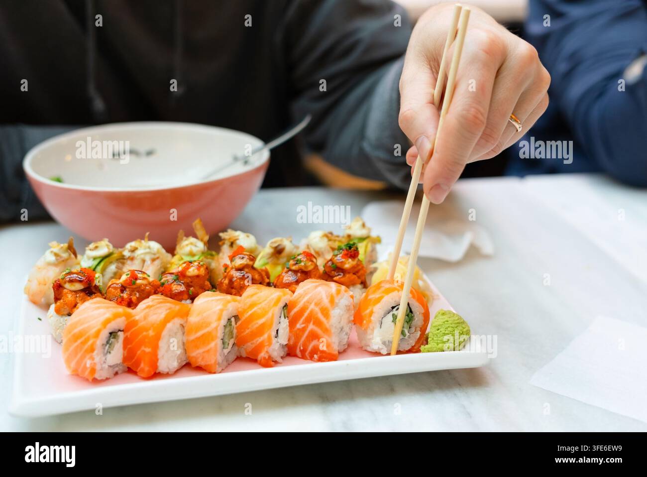 Mann, der Sushi mit Stäbchen in einem gemütlichen japanischen Restaurant aufnimmt. Gast genießt den authentischen Geschmack frischer Rolls während einer sättigenden Mahlzeit. Geschäftsmann genießt traditionelle Küche in einem einladenden Restaurant Stockfoto