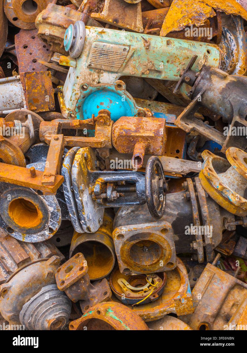 Unordentlicher Haufen verwitterter und verrosteter Industrie-Maschteile, einschließlich Ventile, Rohre, Flansche und Zahnräder. Strukturierter abstrakter Hintergrund zeigt Farben von Rost und gealterter Farbe, die auf ehemalige Nutzung und Verlassenheit hinweisen. Stockfoto