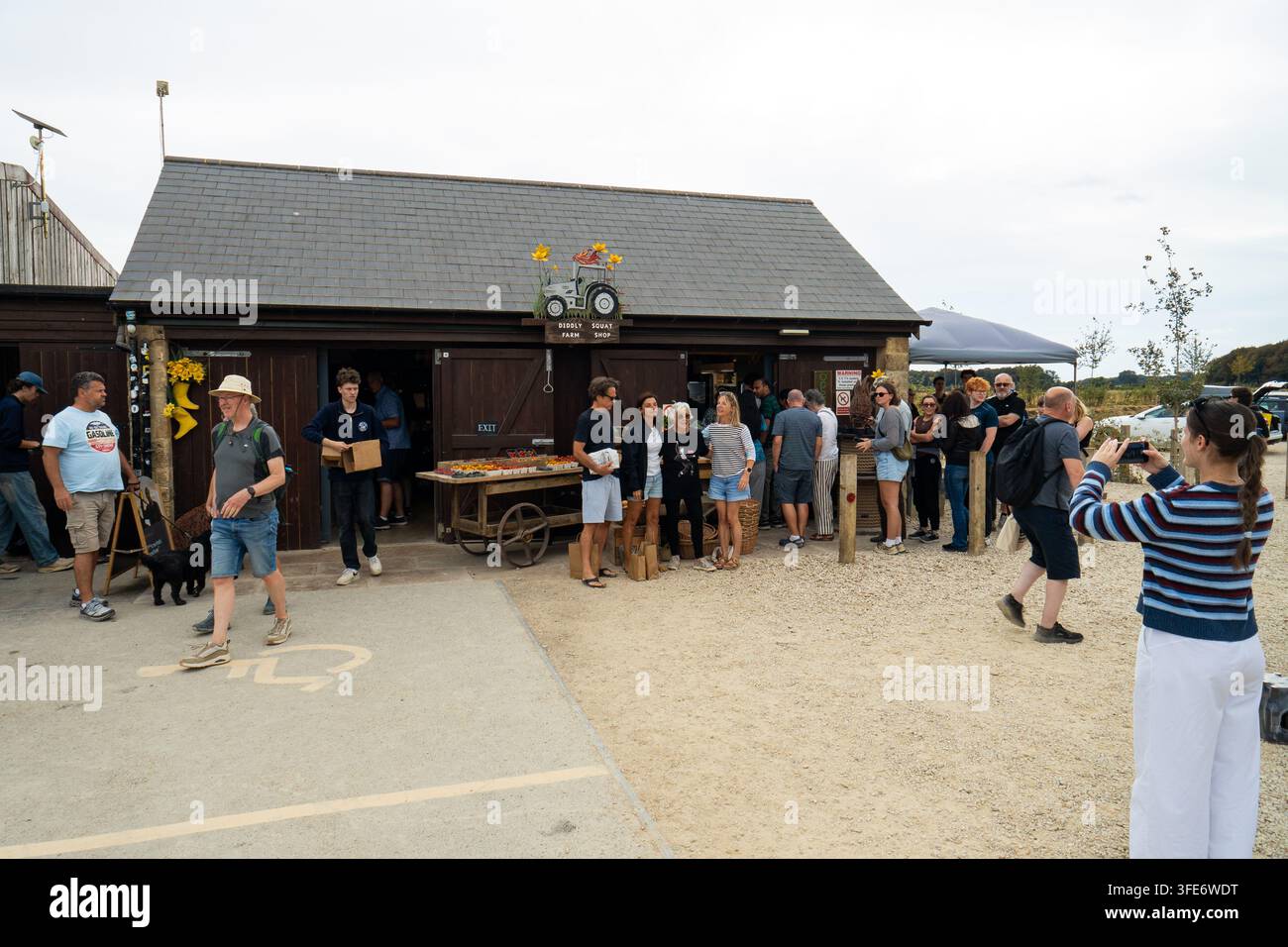 Chipping Norton, Oxfordshire, Vereinigtes Königreich, 17. August 2026. Außenansicht des Diddly Squat Farm Shop mit einer Schlange von Menschen, die Schlange stehen und Fotos machen. Stockfoto
