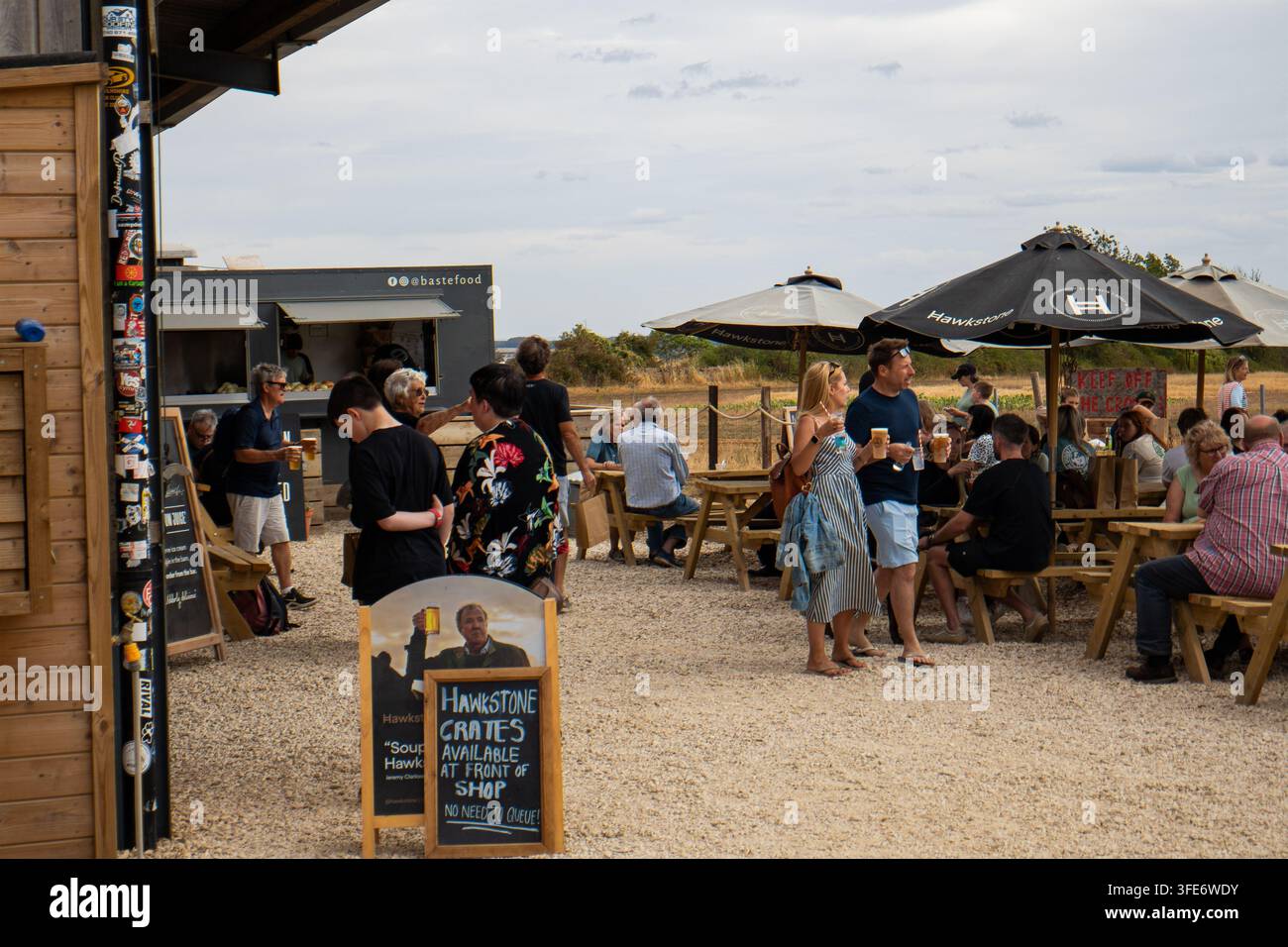 Chipping Norton, Oxfordshire, Vereinigtes Königreich, 17. August 2026. Menschen versammelten sich um Picknicktische und Hawkstone-Bier-Schilder auf der Diddly Squat Farm Stockfoto